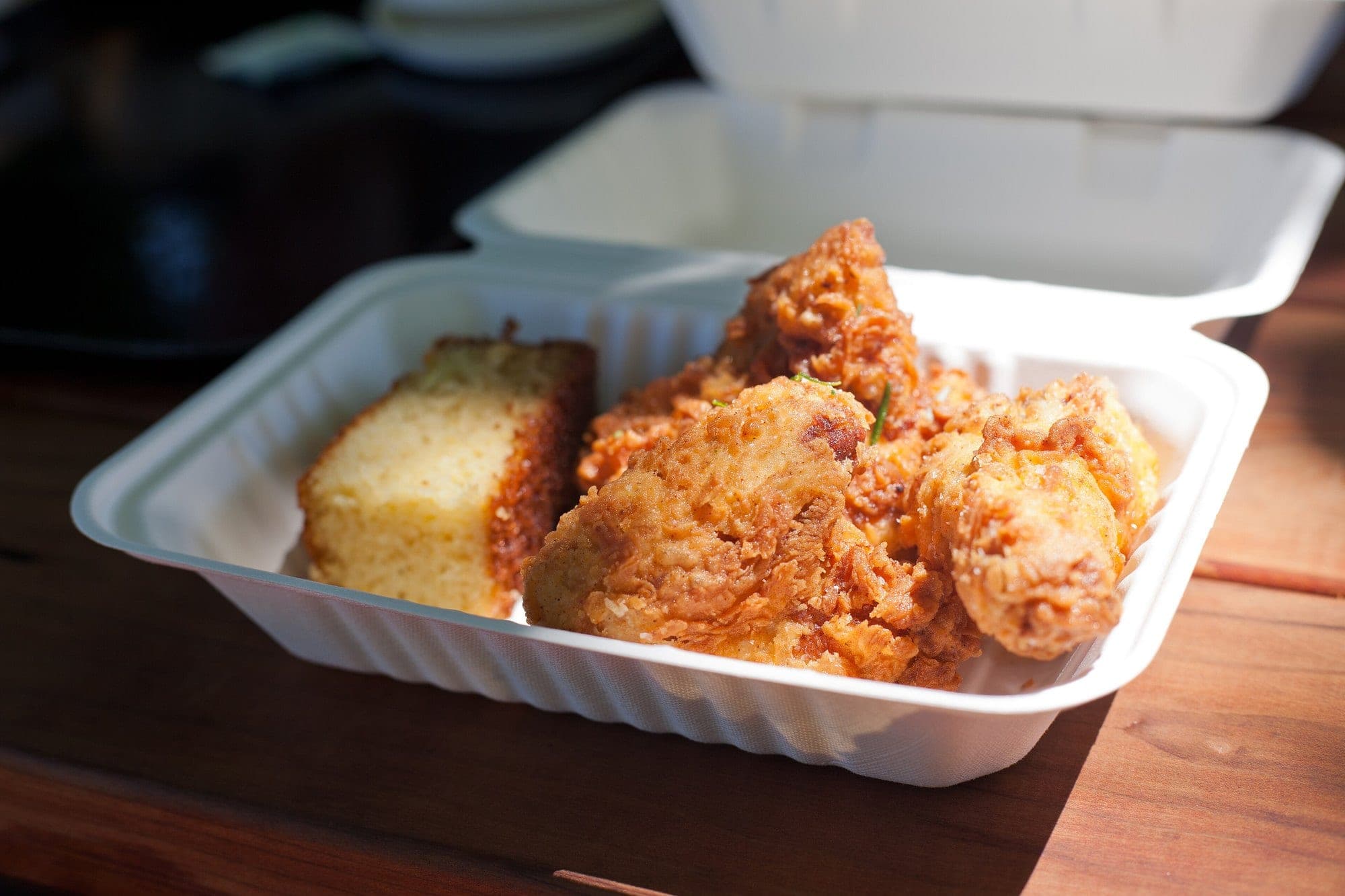 Des morceaux de poulet frit bien dorés dans une barquette, avec un morceau de pain de maïs