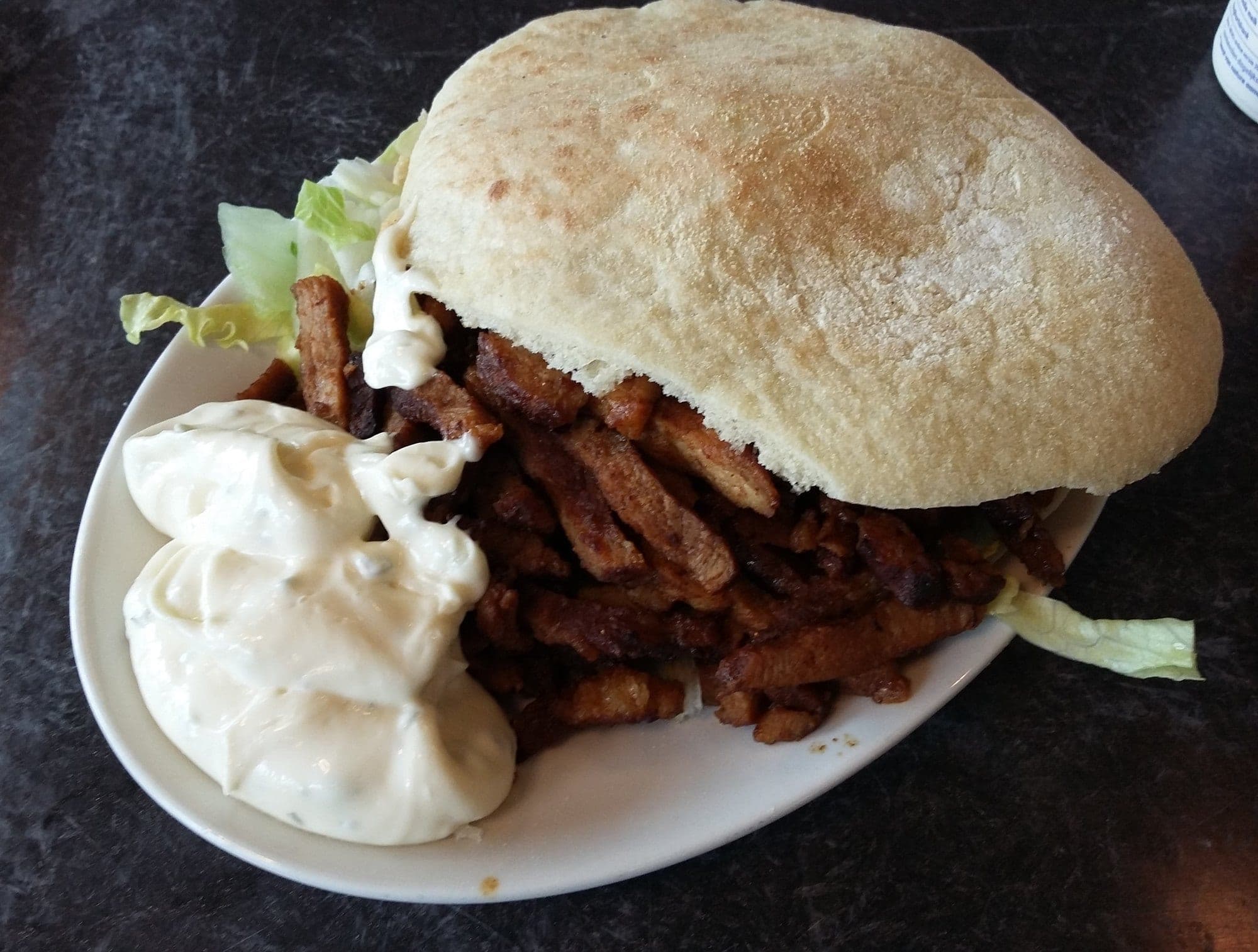 Un pain garni de viande de chawarma, avec de la salade et une sauce blanche à côté