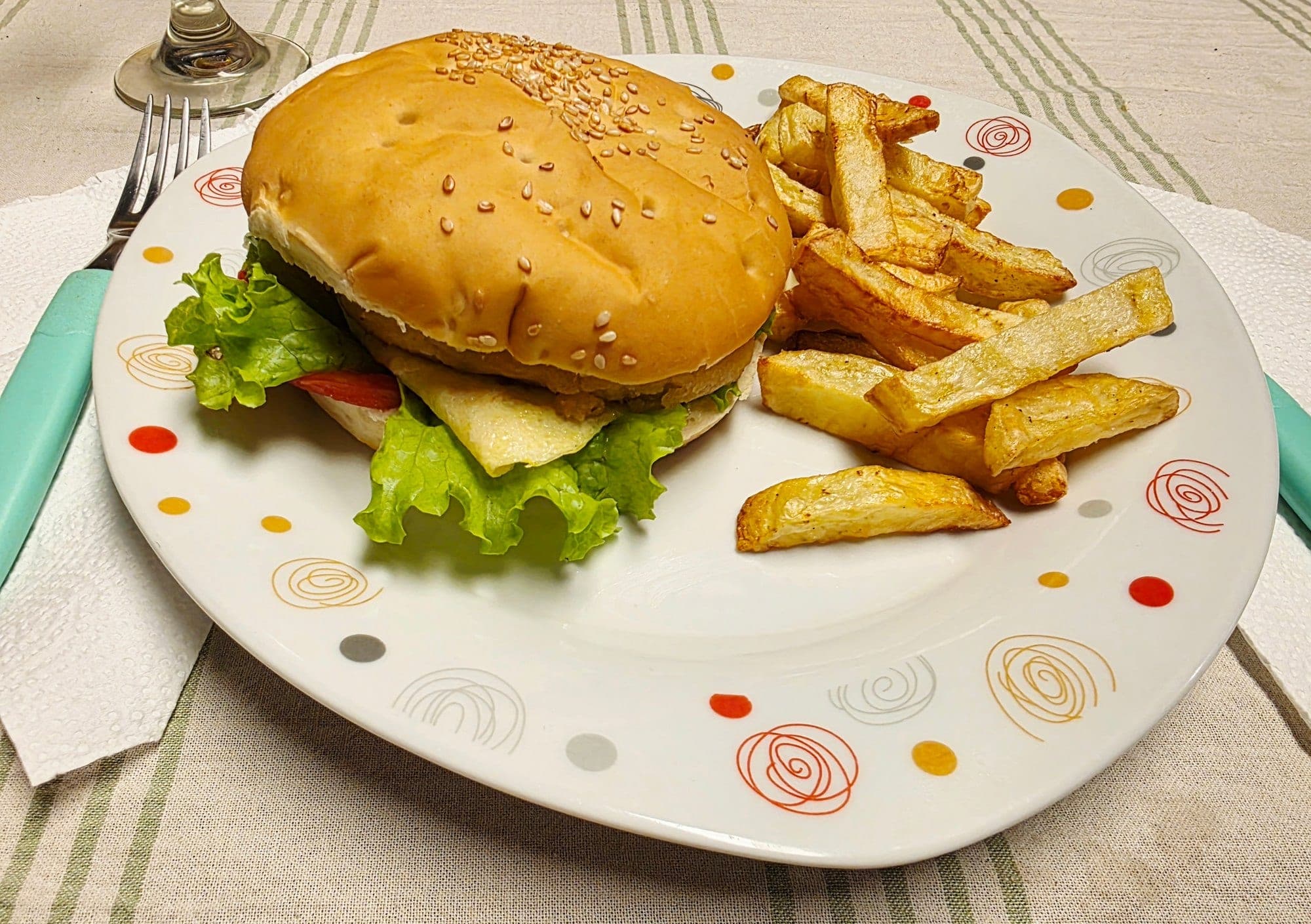Un burger avec salade, tomate et fromage, servi avec des frites dans une assiette