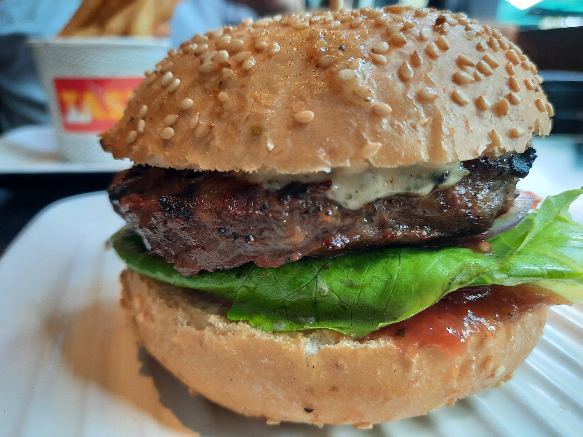Un burger épais avec sa viande grillée, sa salade et sa sauce, vu de près