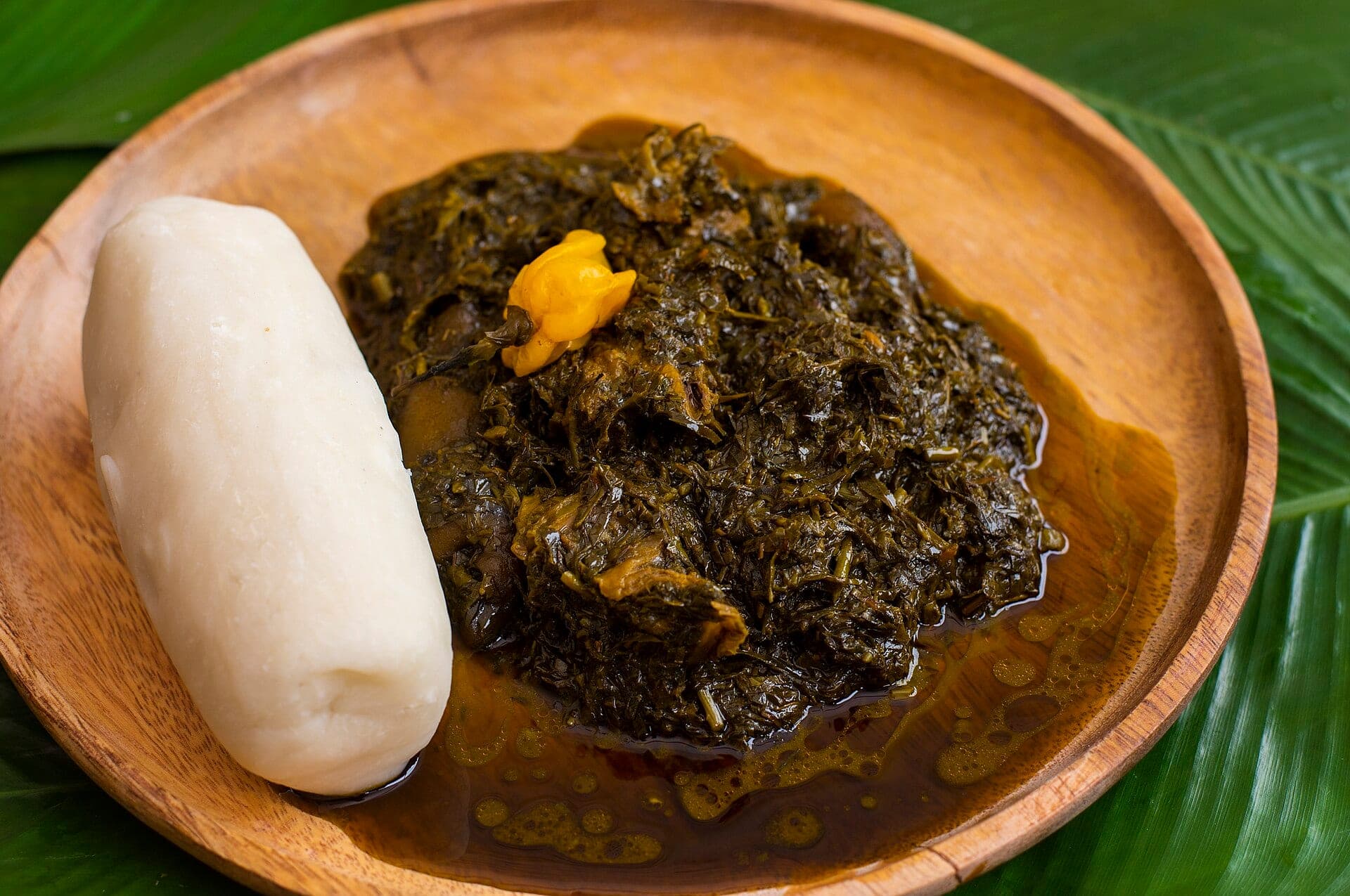 Un plat d’eru dans une assiette en bois, avec une boule de water fufu, posé sur une feuille