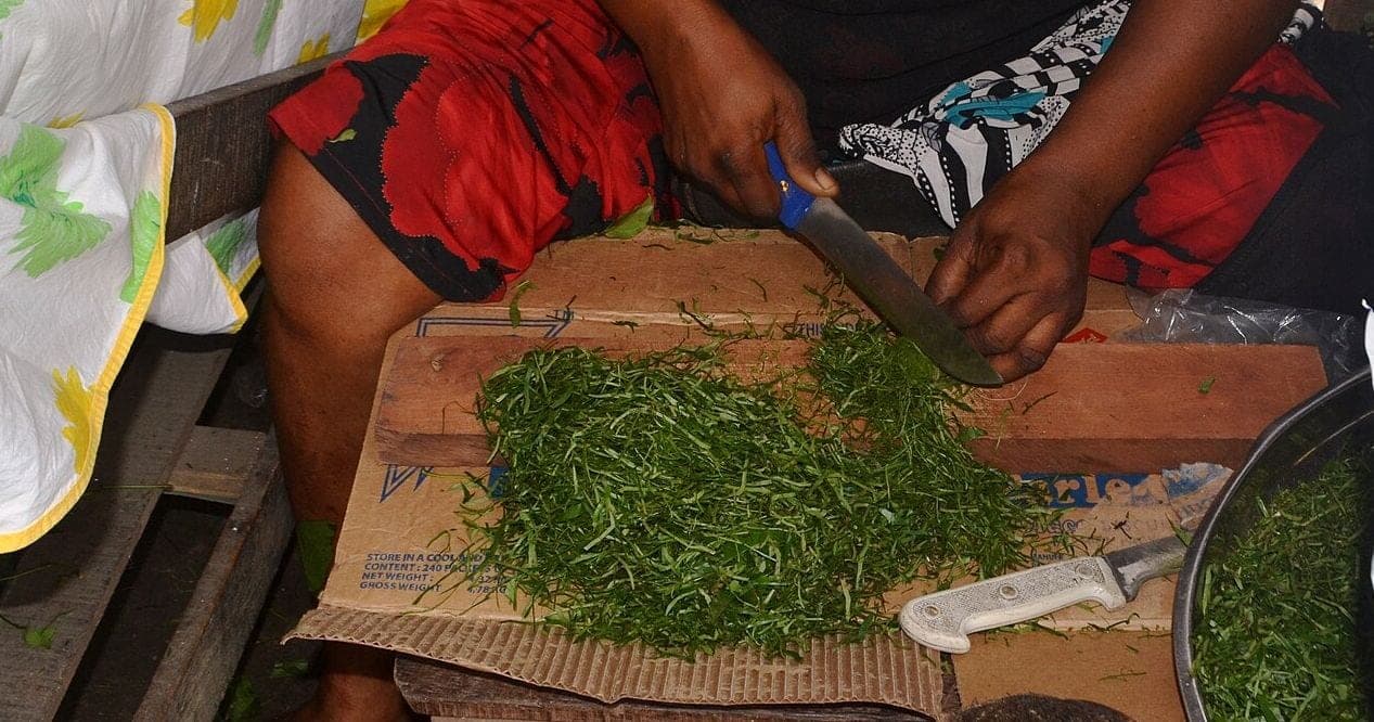 Des mains émincent des feuilles d’eru au couteau, en fils très fins, sur une planche