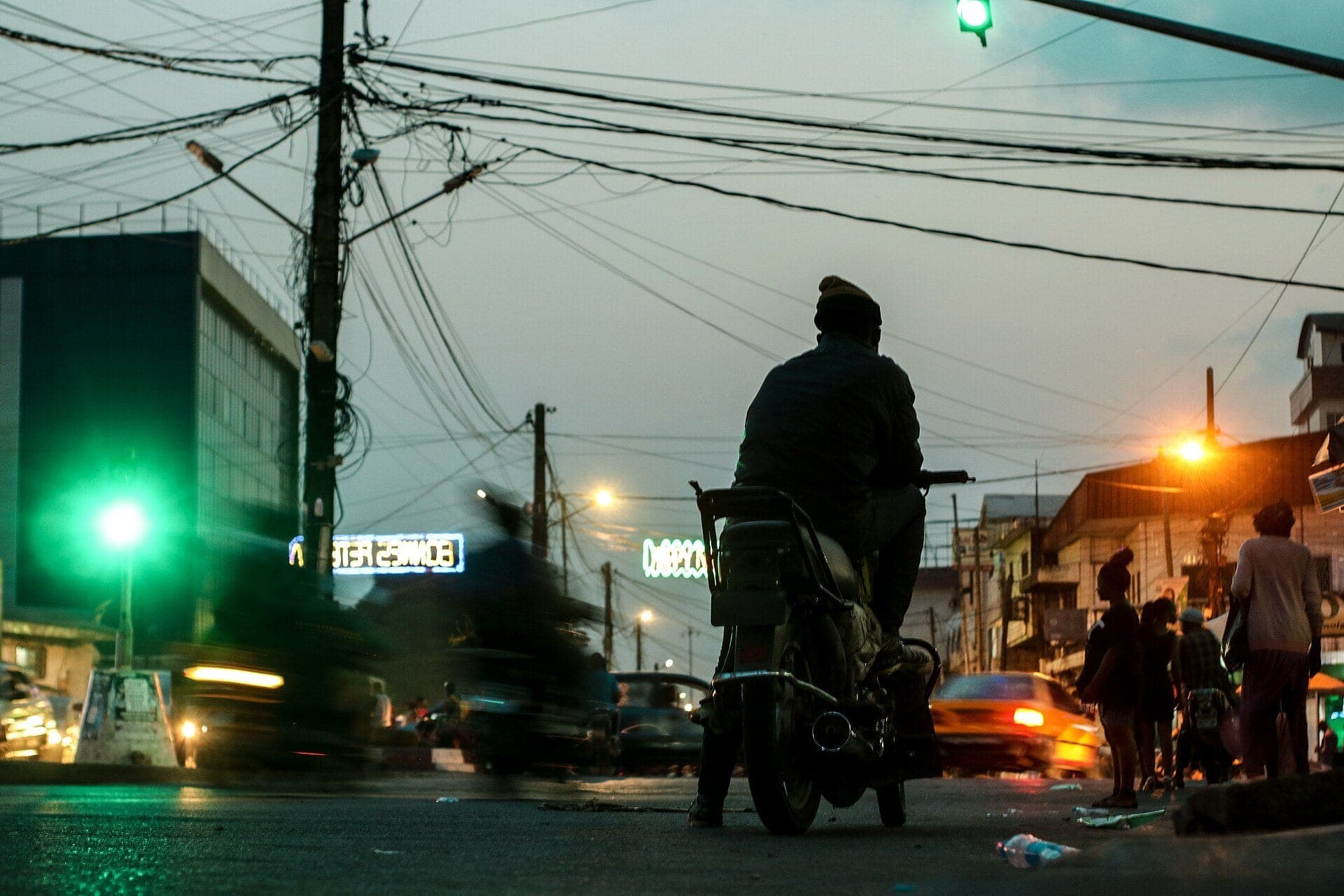Une rue de Douala à la tombée de la nuit, un moto-taxi de dos