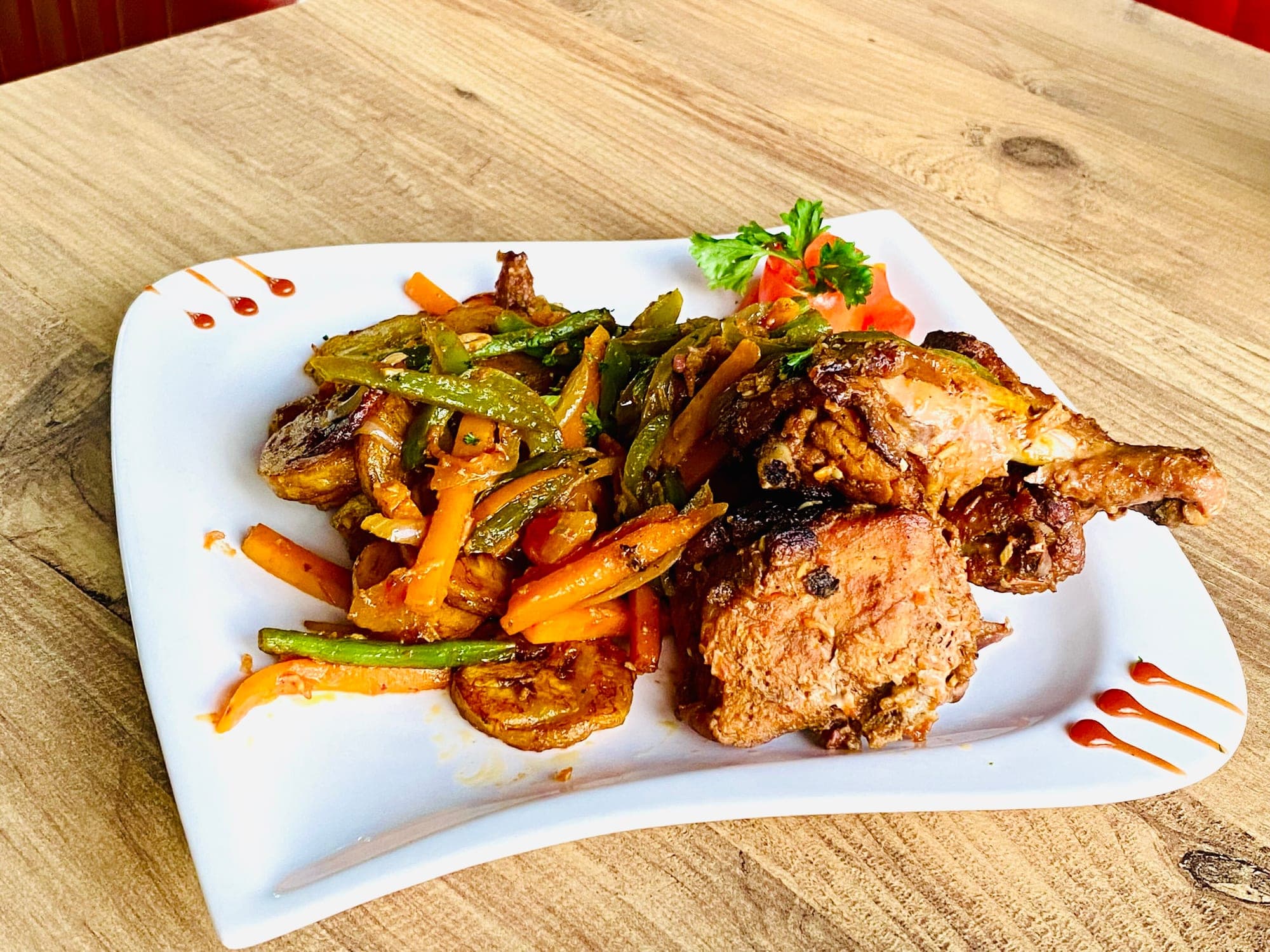 Un poulet DG avec des plantains mûrs frits et des légumes, dans une assiette blanche