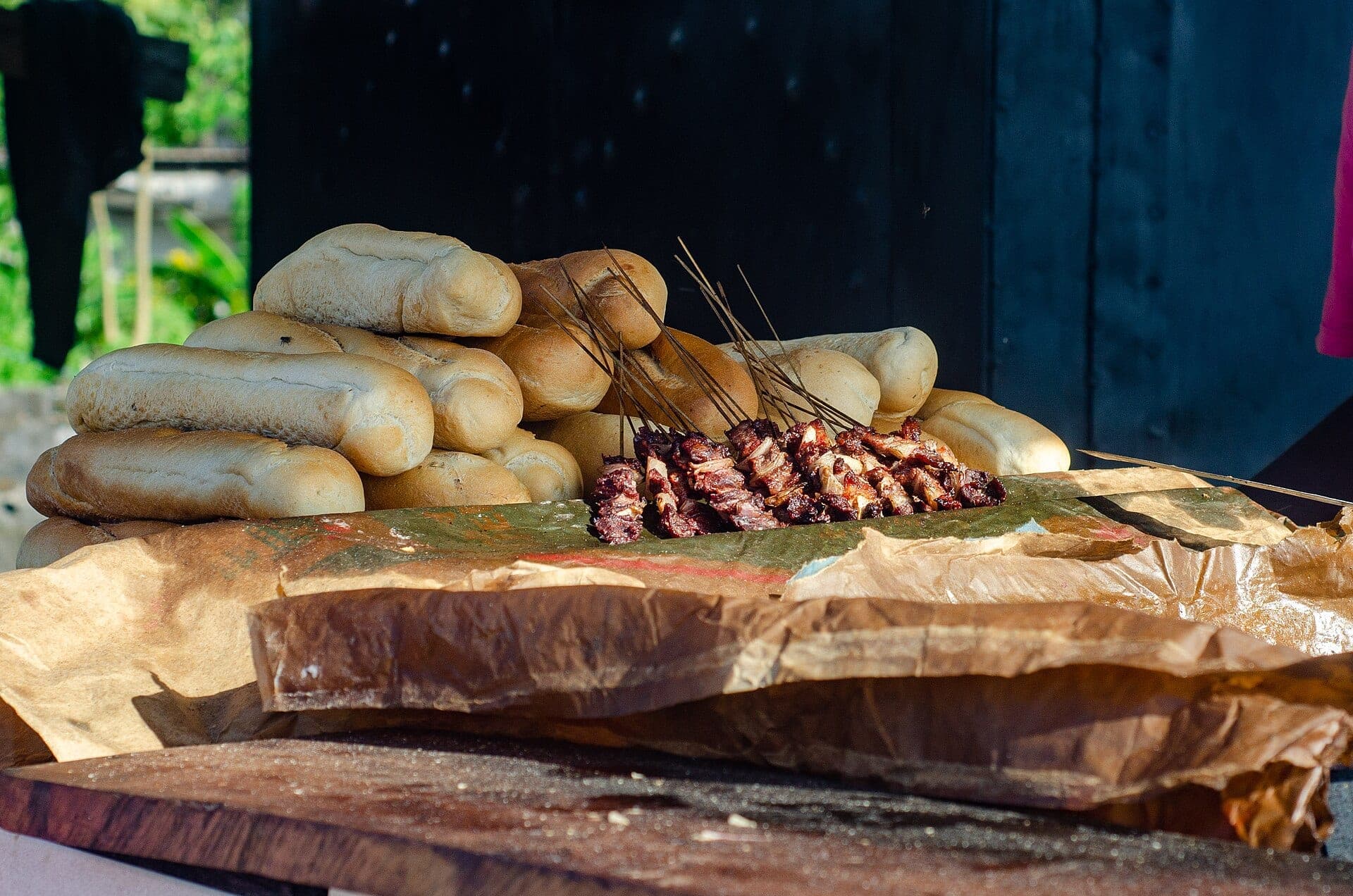 Des brochettes de soya posées sur du papier, à côté de pains