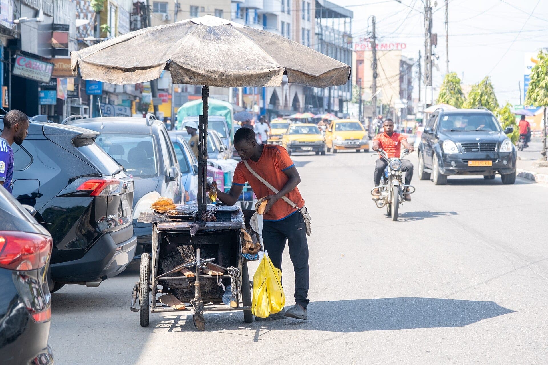 Un vendeur de soya et son chariot sous un parasol, au bord d’une rue