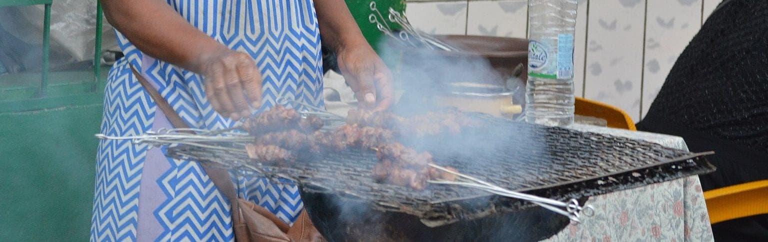 Des brochettes sur une grille, dans la fumée, retournées à la main