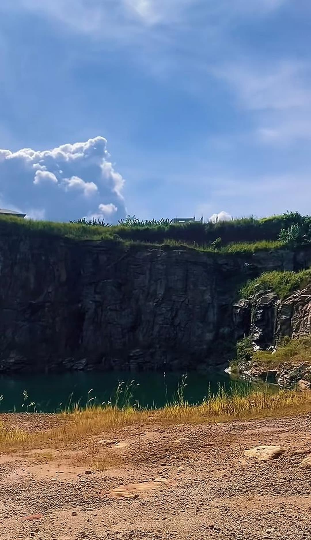 Une paroi de roche sombre au-dessus de l’eau du lac, sous un grand ciel bleu